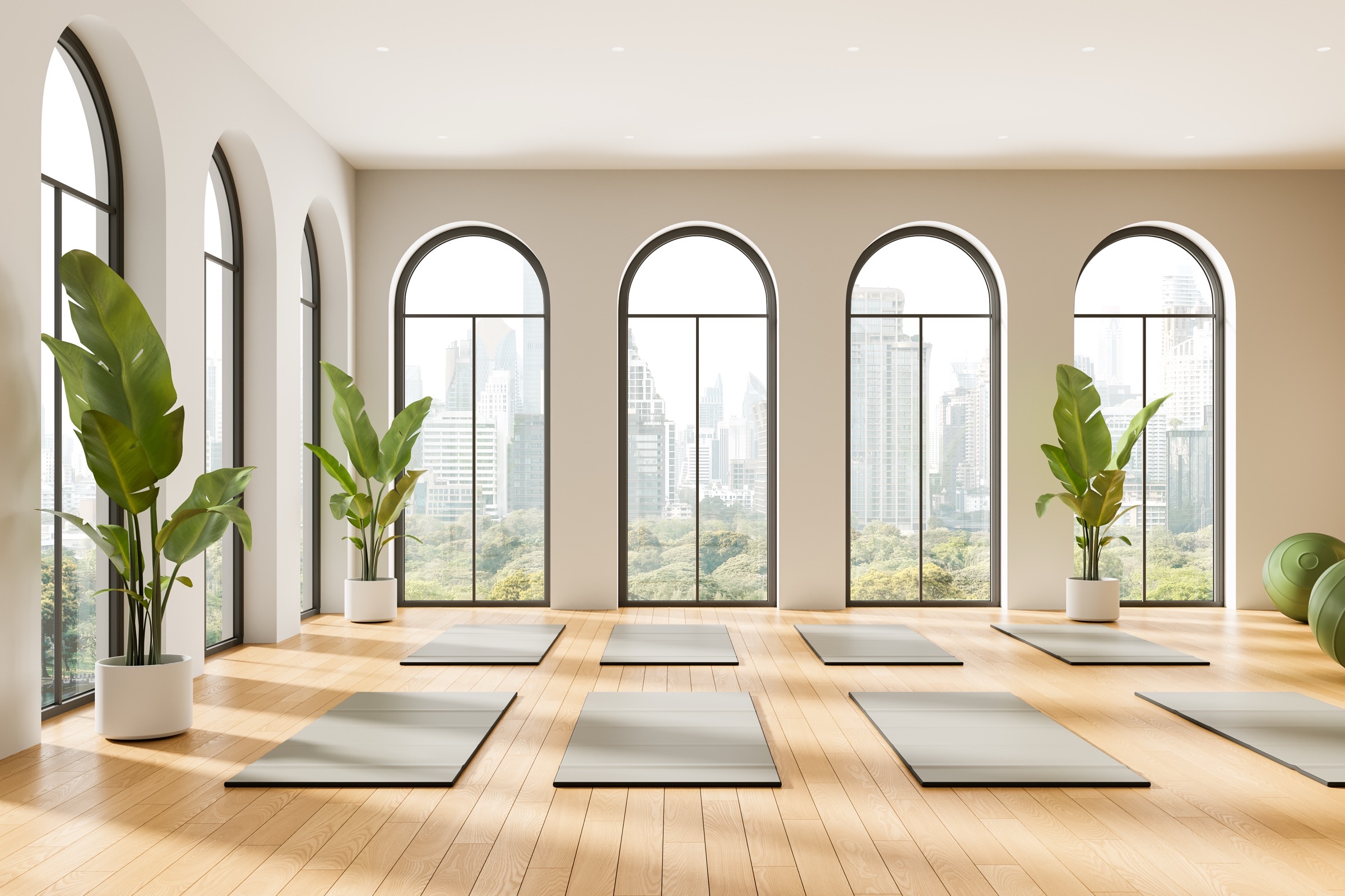 Bright yoga studio with tall arched windows, wood floors, mats, and potted plants